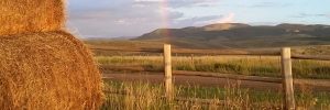 hay by a wooden fence with a rainbow and mountains in the background
